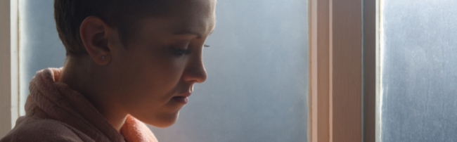 A depressed looking girl standing next to a window.